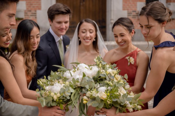 Bride and bridesmaids look down at the flower bouquet in hands